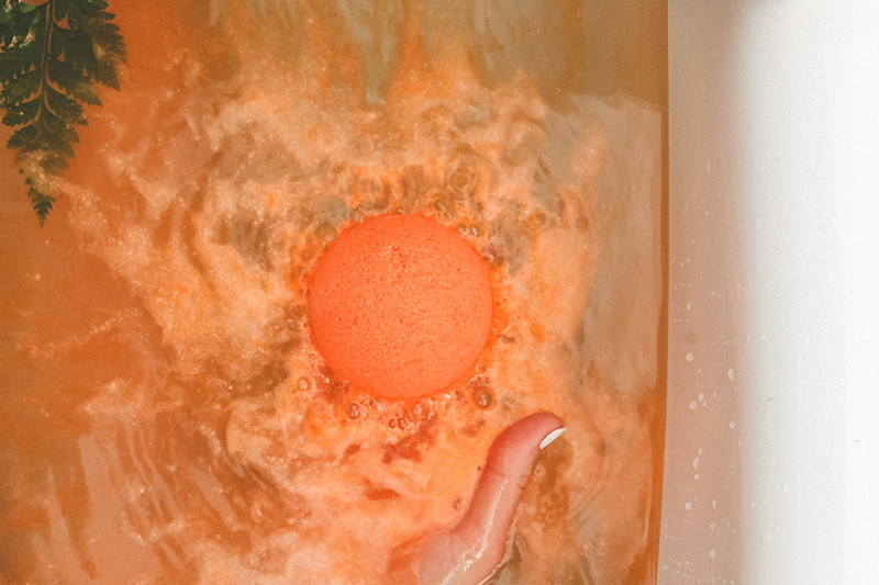Model holding citrus bath bomb while it dissolves in tub.