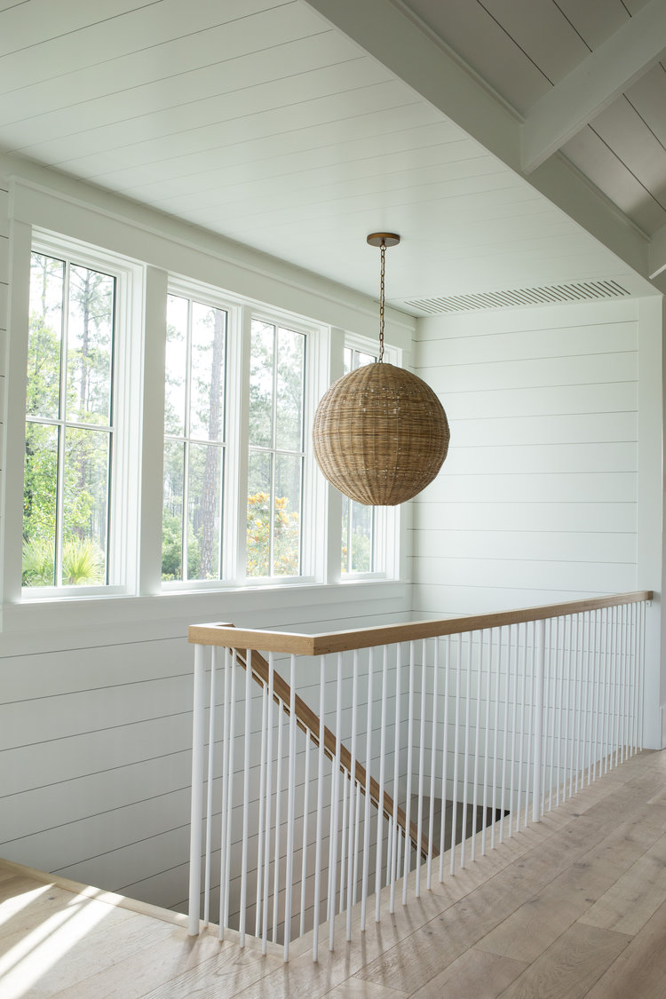 Woven wicker sphere pendant hanging in stairway of lovely modern farmhouse coastal style cottage by Lisa Furey.