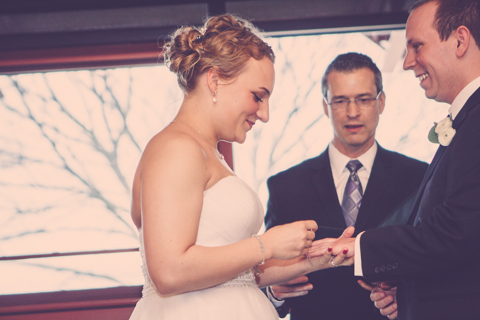 bride places wedding ring on groom's hand as officiant looks on in Columbus
