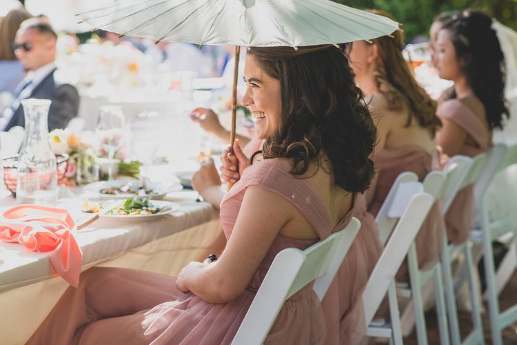 Last Minute Checklist: Things To Know Before Your Outdoor Wedding - A Bridesmaid Using A Parasol To Shield Herself From The Summer Heat During An Outdoor Wedding Reception.