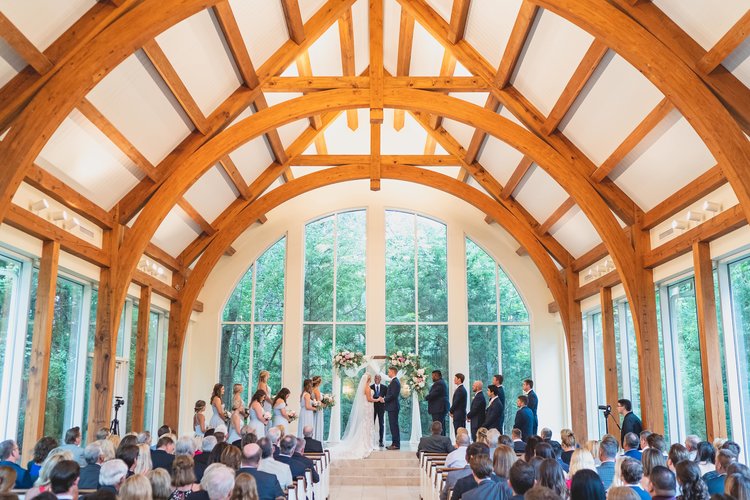 Wedding Ceremony In A Chapel With Wooden Arches Decorating The High Vaulted Ceiling.