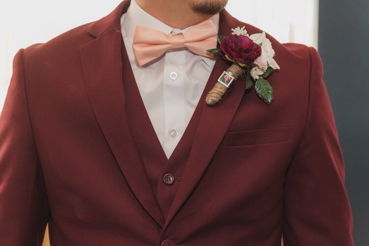 Groom Wearing A Deep Red Tuxedo, A Pink Bow Tie And A Boutonniere With Twine Shaped Like A Cigar.