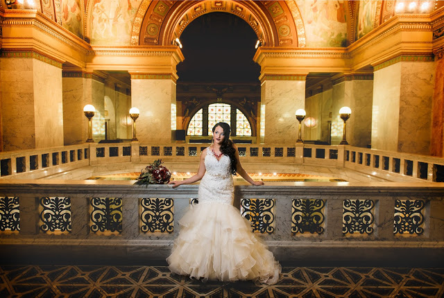 a woman in a white wedding dress is framed by an arch in a magnificent building with warm tungsten tones