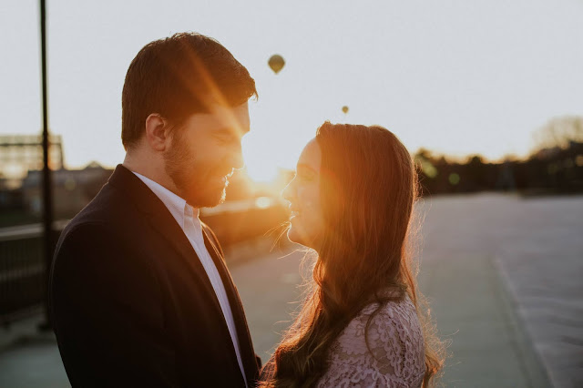 the sun is setting behind a couple on a bridge in indianapolis and the couple is positioned so the sun is in between them and there is a flare