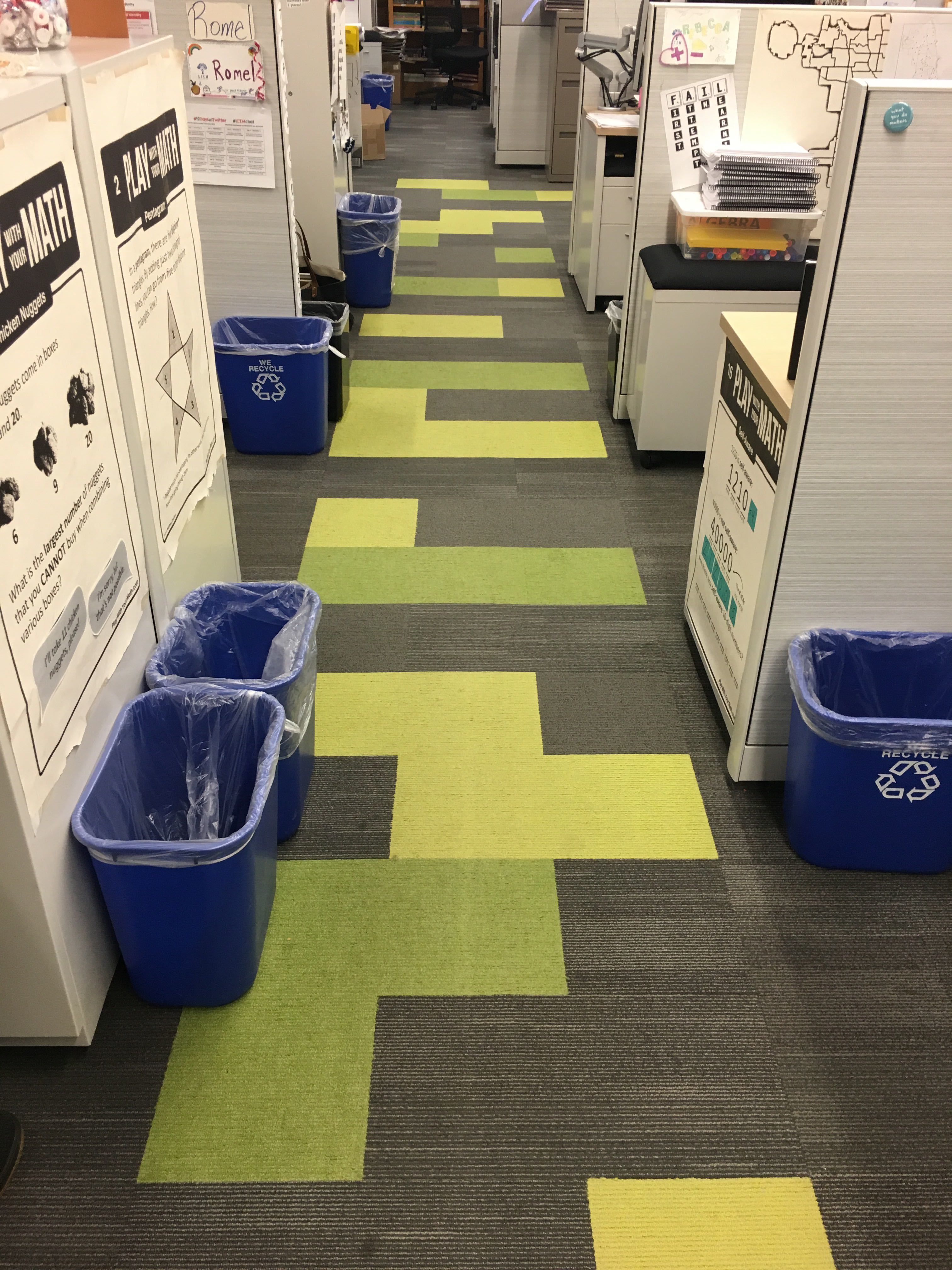 An office with cubicles, recycling bins, and a Tetris-like grey, yellow, and green carpeting scheme.