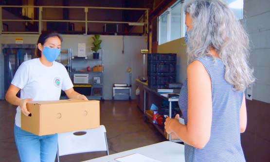 A female foodhub employee is bringing a box of Hawaii grown fruits and vegetables to a customer for purchase at Farmlink Hawaii, a foodhub located in Honolulu, Hawaii.