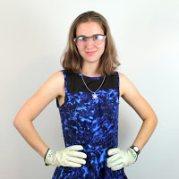 Erin Winnick wearing a safety glasses, lab gloves, and a blue dress she sewed