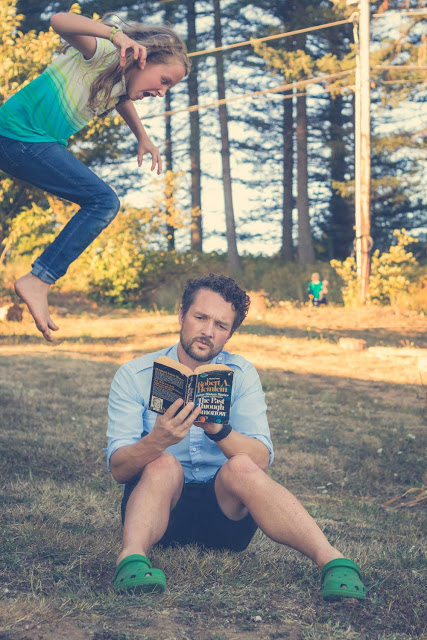Daughter leaping over her father while he reads in the grass