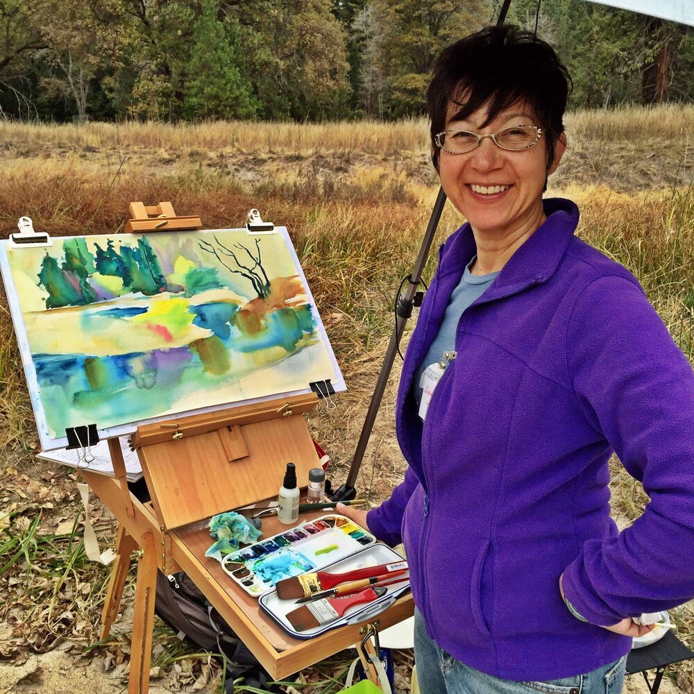 Cassandra Nguyen Musto stands in a meadow in Yosemite with her easel and a painting she is working on