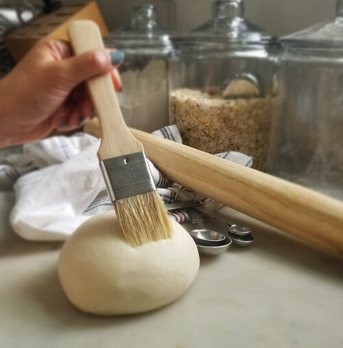 dough being brushed with a pastry brush and baking utensils in the background