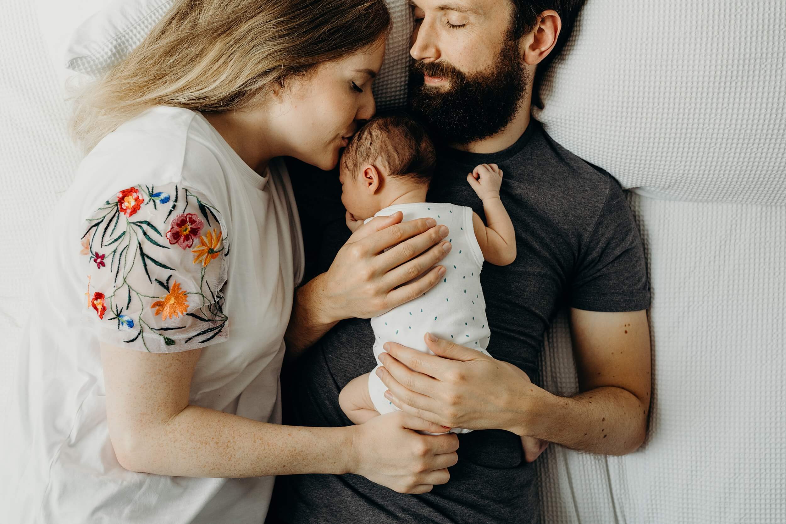 Parents cradle their newborn baby while lying on the bed relaxed natural Newborn Photography Glasgow