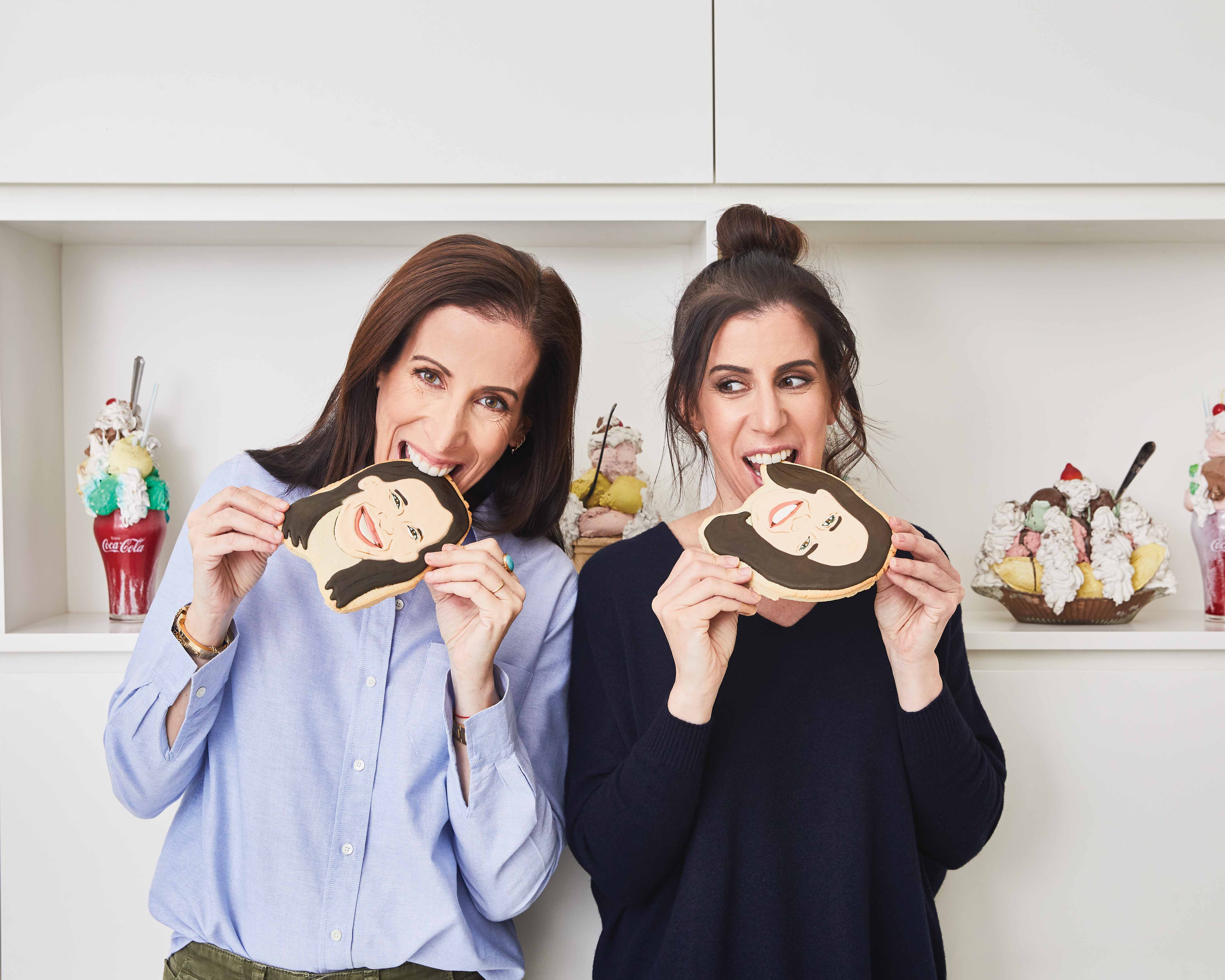 Julie and Lisa biting on cookies with their faces on them