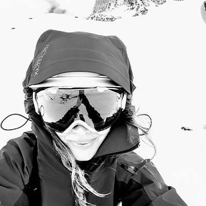 Katie is smiling with snowboarding googles, and a winter jacket on while on a snowy hill.