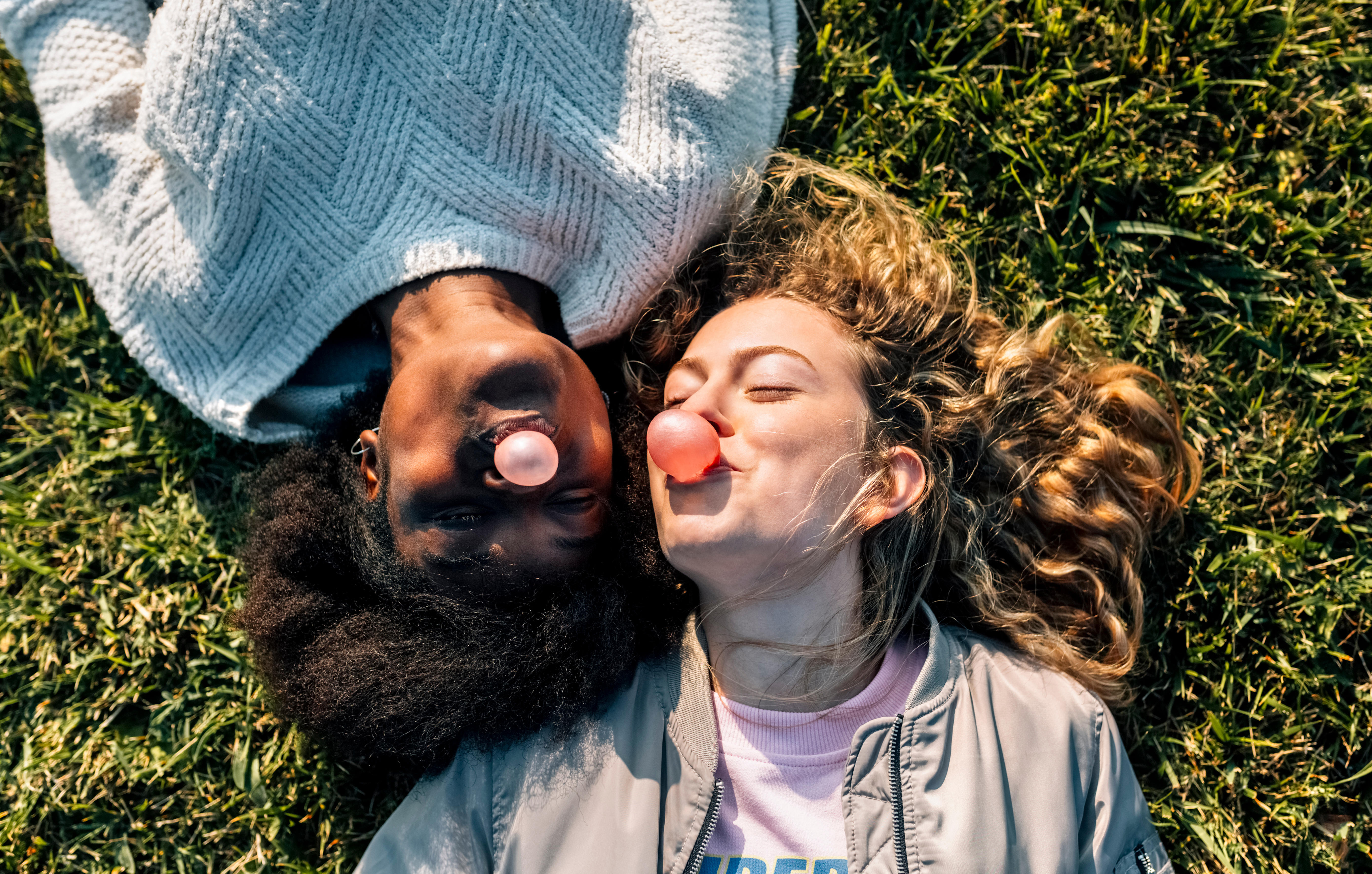 Two girls blowing bubblegum in grass 