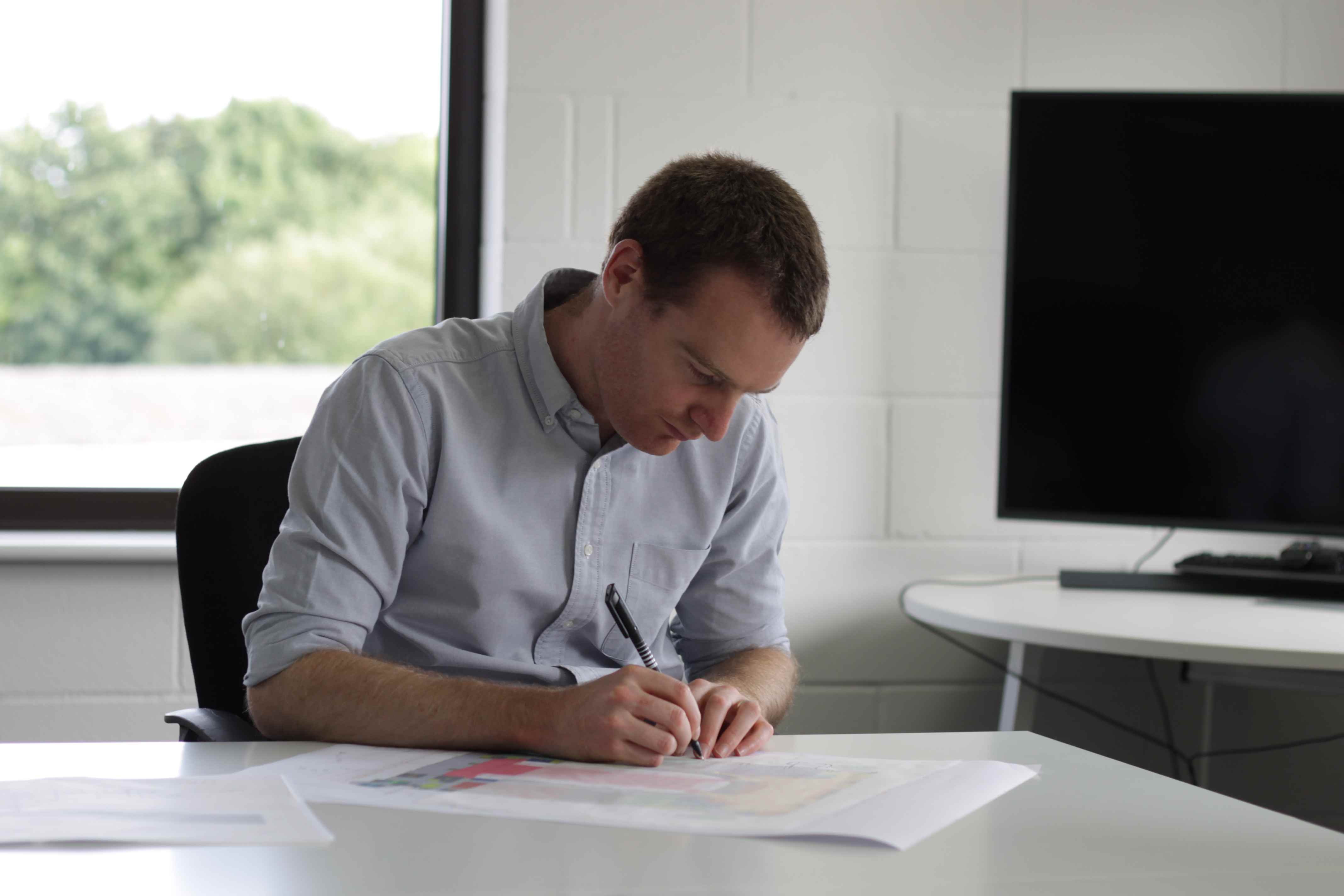 A photo of Joe Dimery, sketching over a layout drawing using tracing paper