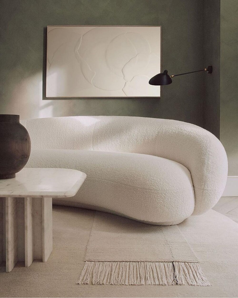 un canapé arrondis avec un tissu en laine bouclée, mur vert et couleurs naturelles