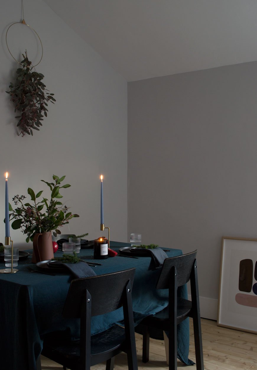 Moody and minimal Christmas table styling with a blue table cloth, black dinner plates and natural winter foliage