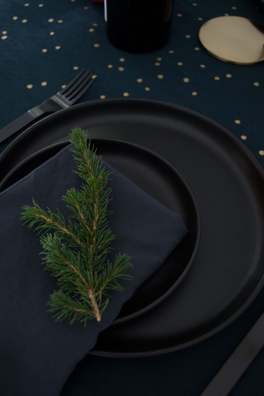Using black kitchen dinner plates to create a moody and minimal Christmas table setting topped with winter foliage
