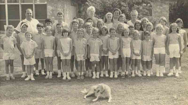 Black and white photo of student body group shot. A pet dog included. Students are all wearing white shorts and school blouses.