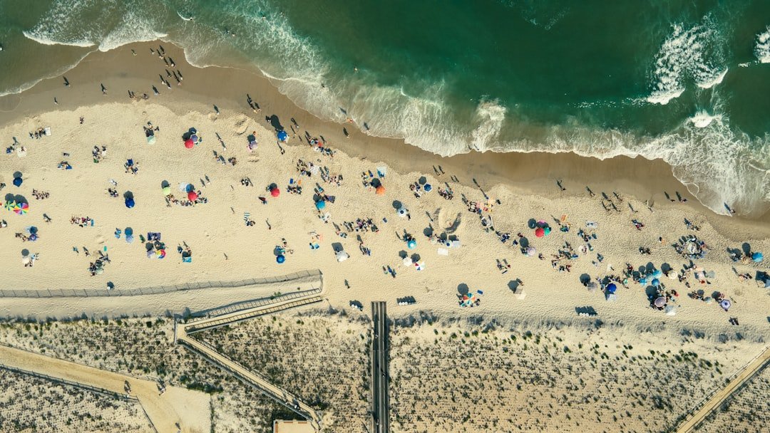 Bird's eye view of blue and green ocean and sandy beach dotted with umbrellas, chairs, and people in Beach Haven Crest, LBI.