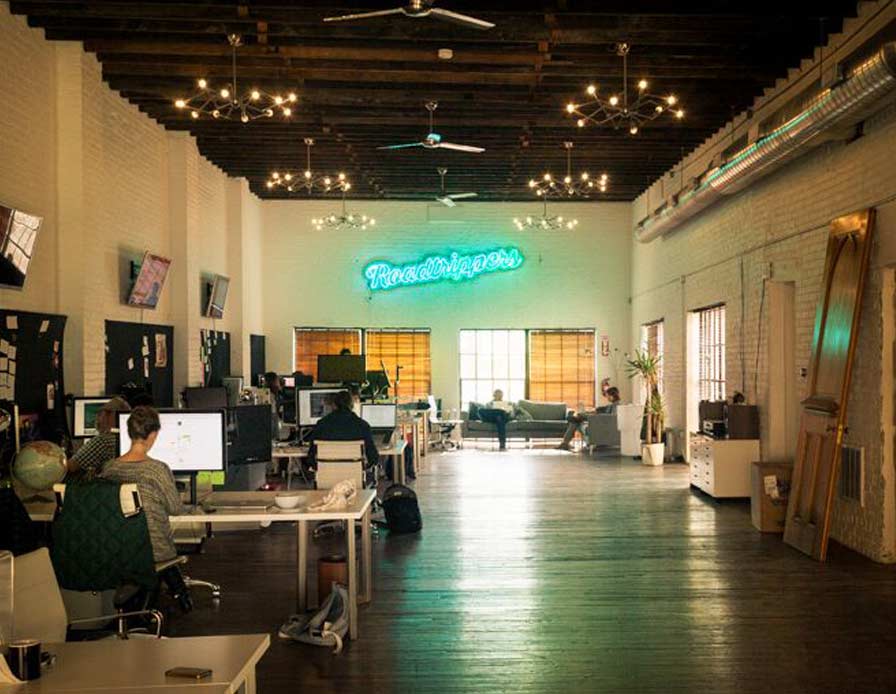 office space with desks and a large neon sign that says Roadtrippers