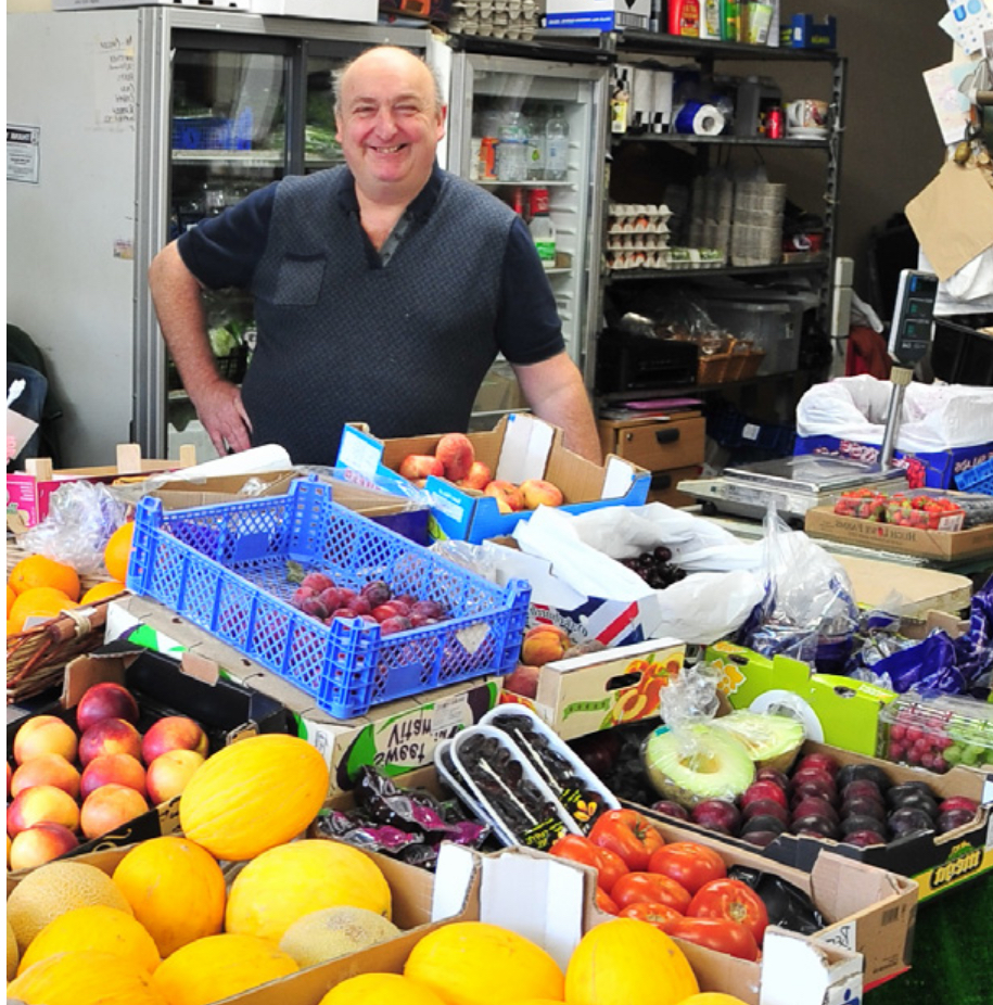 Smiling green grocer behind a counter