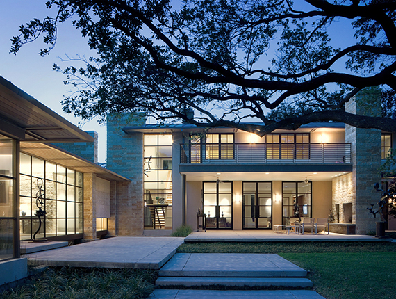 Contemporary home at dusk is illuminated lighting up beautiful sculptures and exterior terraces.